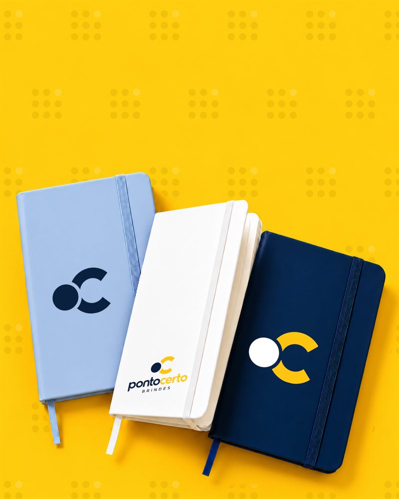 Três cadernetas emborrachadas azul-claro, branca e azul-marinho com a logo ou o símbolo da Ponto Certo Brindes na capa.